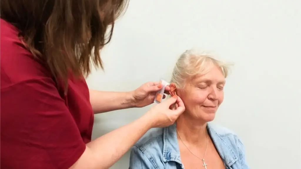 A social nurse performing ear acupuncture according to the NADA protocol on a relaxed woman.